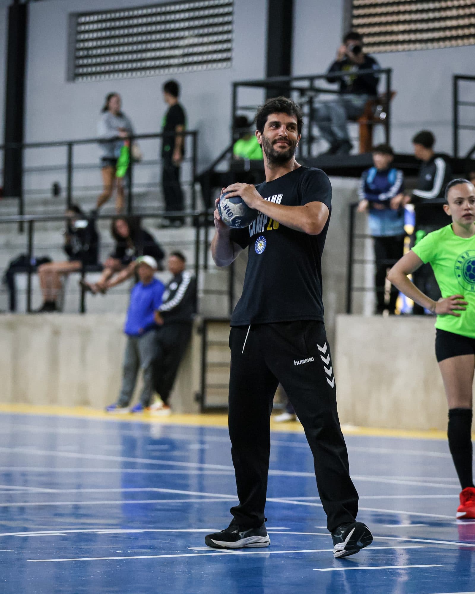 Treinador convidado com a bola na mao no meio da quadra, turma observando