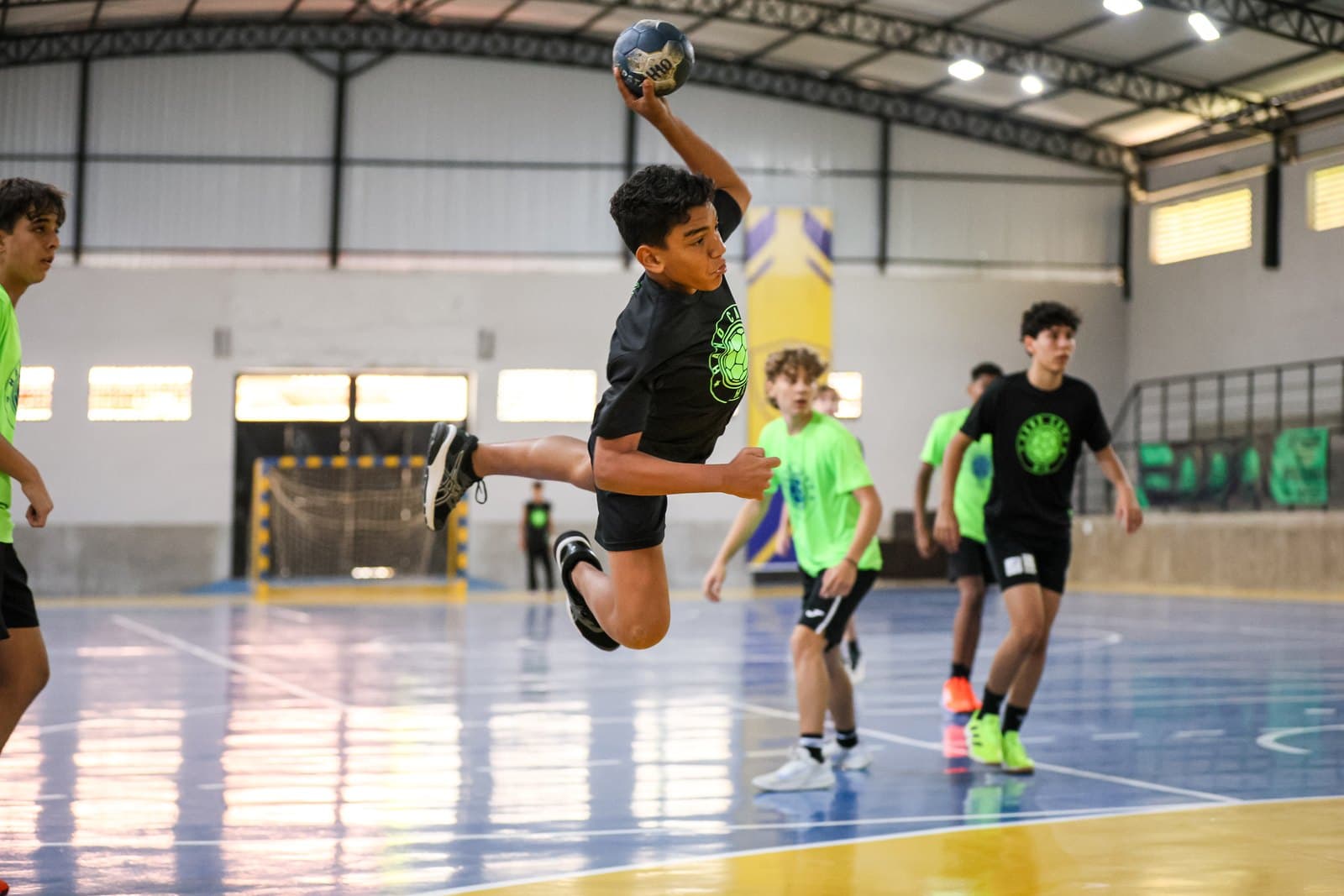 Arremesso em suspensao durante partida na quadra, com o time observando ao fundo