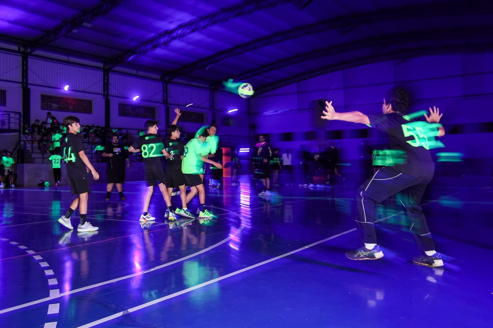 Jogo sob luz negra a noite: atletas disputando a bola com rastro de luz verde